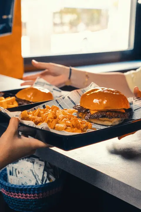 Tablett mit zwei Burgern und Pommes wird über den Tresen gereicht